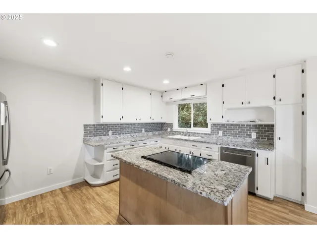 a kitchen with granite countertop a sink a stove a refrigerator and white cabinets