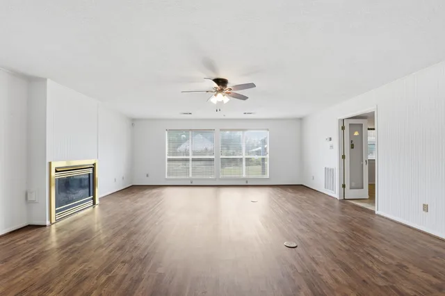an empty room with wooden floor a ceiling fan and windows