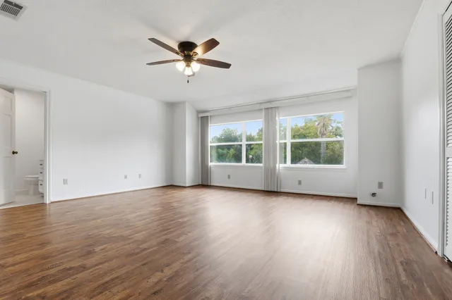 an empty room with wooden floor fan and windows