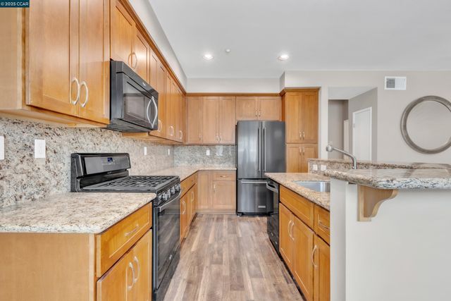 a kitchen with stainless steel appliances granite countertop a sink a stove a refrigerator a washer dryer and white cabinets