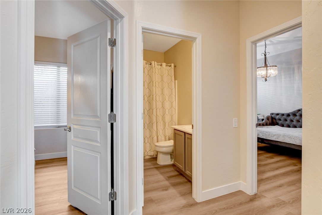 2649 Rue Marquette Avenue Henderson, NV 89044 - Photo 29 of 55 This image shows a hallway with open doors leading to a bathroom, a room with a window, and another room featuring a chandelier.