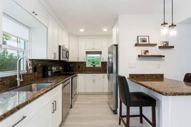 a kitchen with stainless steel appliances granite countertop a stove top oven a sink a refrigerator and white cabinets