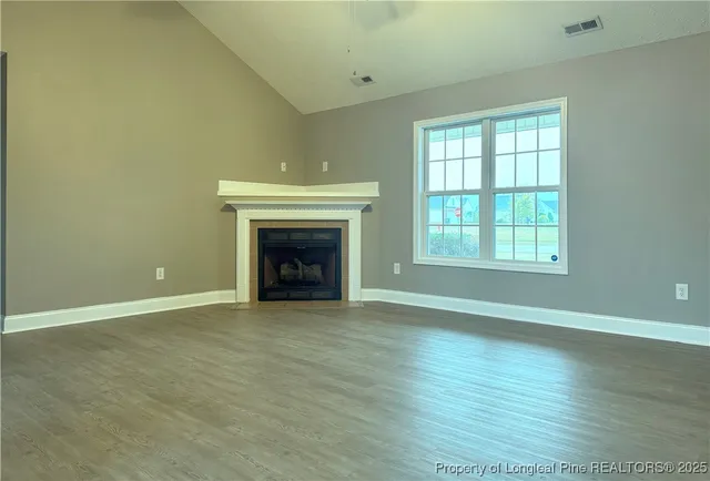 an empty room with wooden floor fireplace and windows