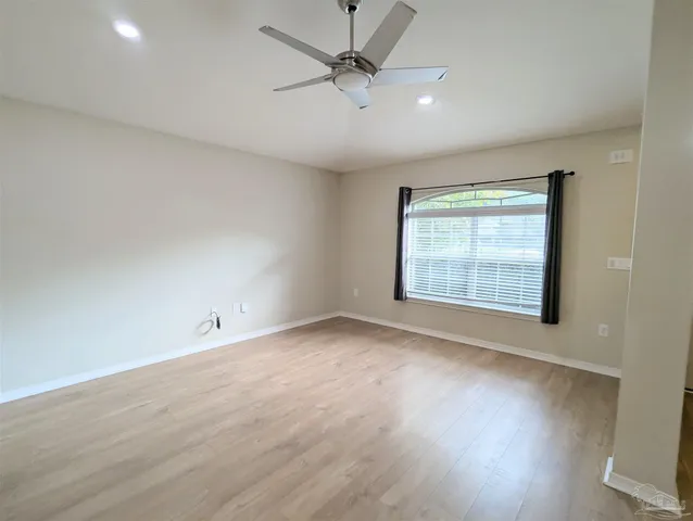 an empty room with wooden floor ceiling fan and windows