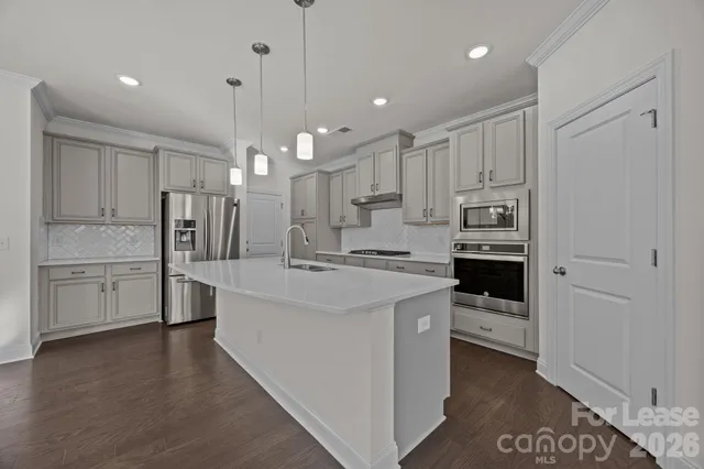 a kitchen with stainless steel appliances kitchen island granite countertop a refrigerator a sink a stove and white cabinets with wooden floor