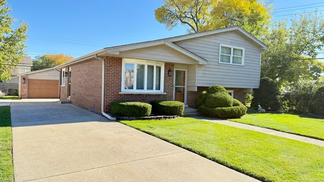 a view of a house with a yard plants and large tree