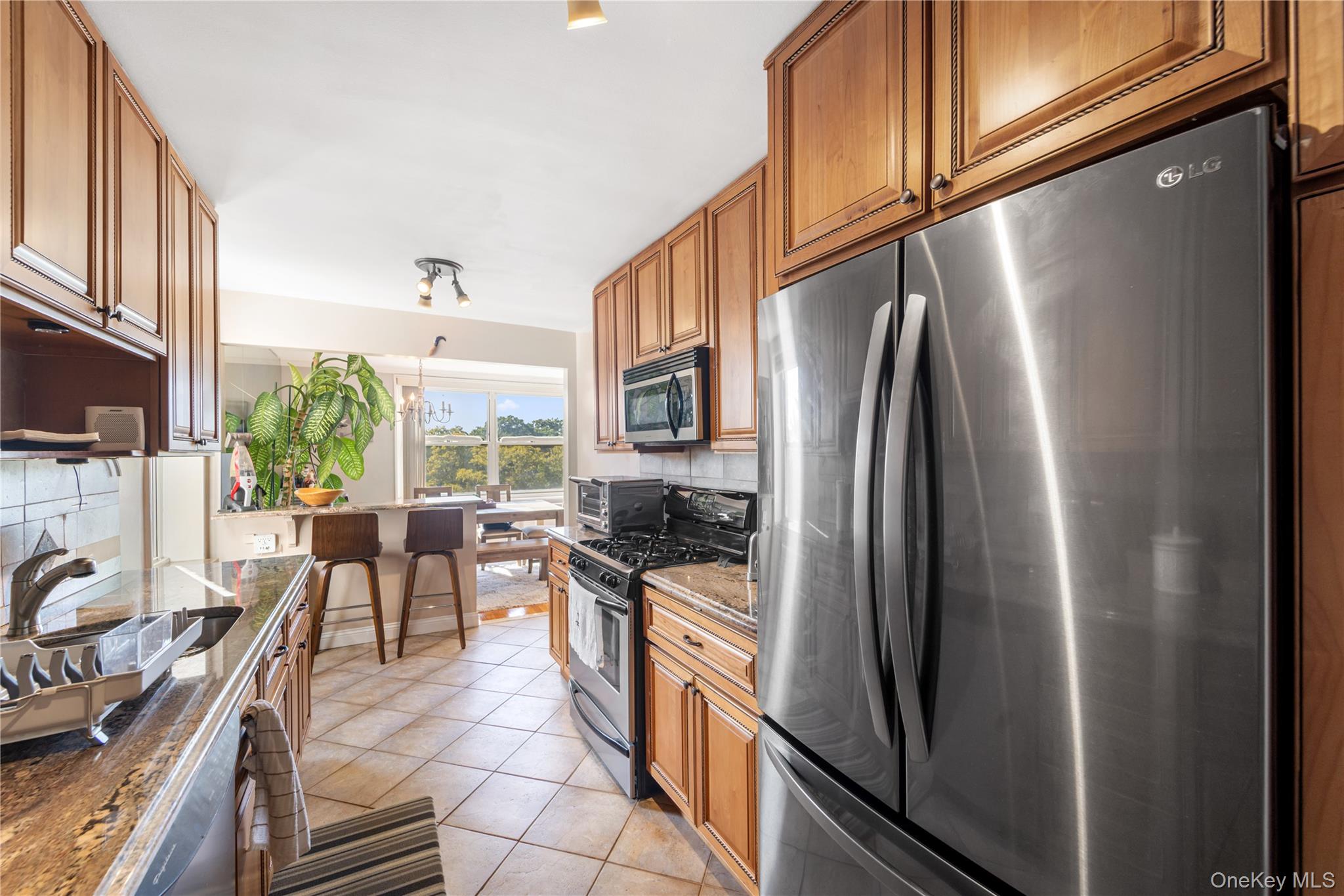 211-40 18th Avenue, Unit 6J Queens, NY 11360 - Photo 8 of 26 a kitchen with stainless steel appliances granite countertop a refrigerator a stove top oven a sink and dining table with wooden floor