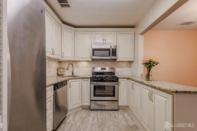 a kitchen with stainless steel appliances granite countertop a stove a sink and white cabinets