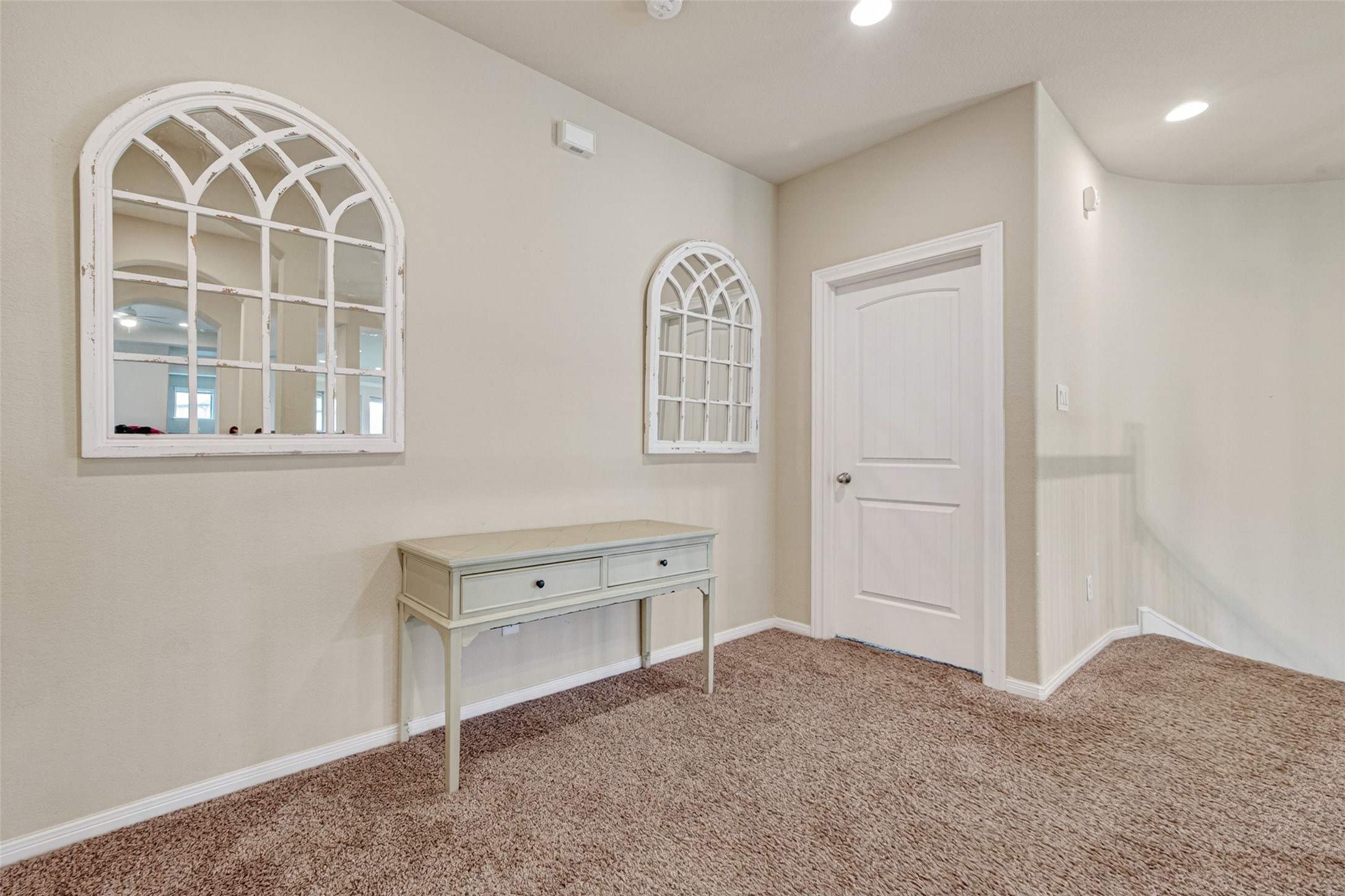 25611 Ellis Ridge Court Katy, TX 77494 - Photo 34 of 49 This photo shows a cozy hallway with carpeted flooring and soft beige walls. It features two decorative arched mirrors and a small console table. The area is well-lit with recessed lighting and includes a white door, offering a welcoming and stylish entrance.
