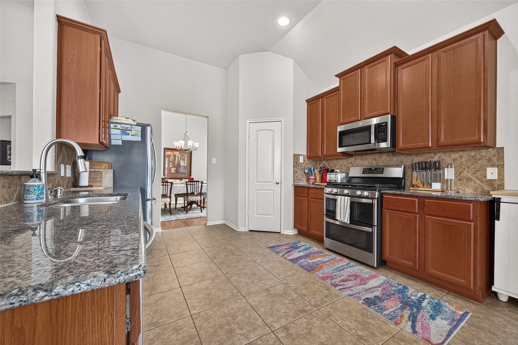 4910 Culver Lane Rosenberg, TX 77471 - Photo 4 of 50 This kitchen features modern stainless steel appliances, including a gas range with double oven, (one being convection,) and microwave. It has ample 42" wood cabinetry and granite countertops, with a tile backsplash and floor. The open layout leads to a dining area, providing a spacious and functional cooking environment.