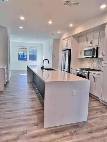 a living room with stainless steel appliances granite countertop a couch a sink a refrigerator and a stove