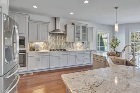 a kitchen with stainless steel appliances granite countertop sink stove refrigerator and wooden floor