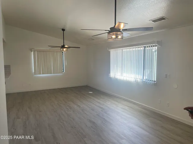 an empty room with wooden floor chandelier fan and windows