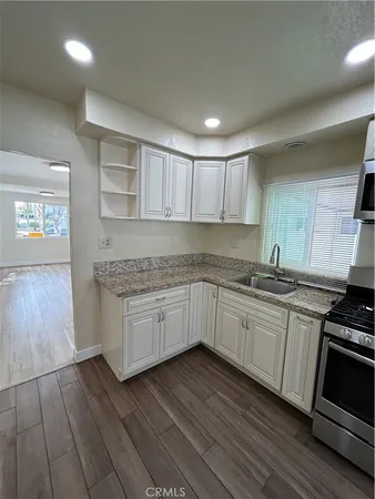 a kitchen with stainless steel appliances granite countertop a stove top oven a sink dishwasher and a microwave oven on the wooden floor