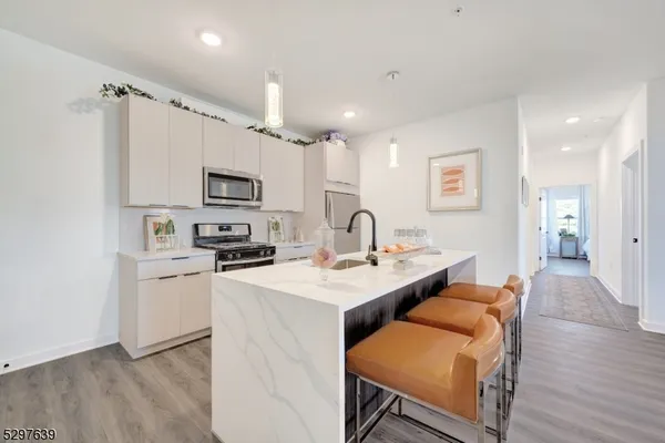 a kitchen with stainless steel appliances granite countertop a sink a stove a refrigerator cabinets and a dining table with wooden floor