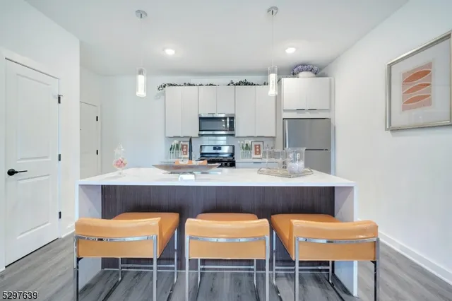 a room with stainless steel appliances kitchen island granite countertop a dining table chairs and a refrigerator
