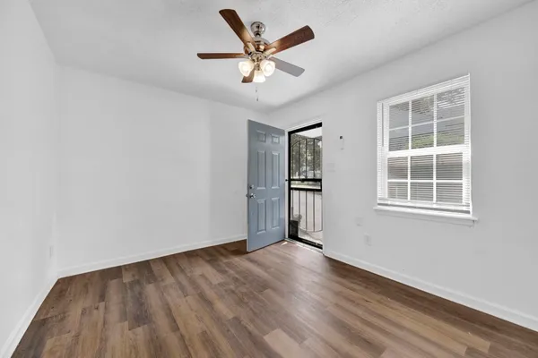 an empty room with wooden floor chandelier fan and windows