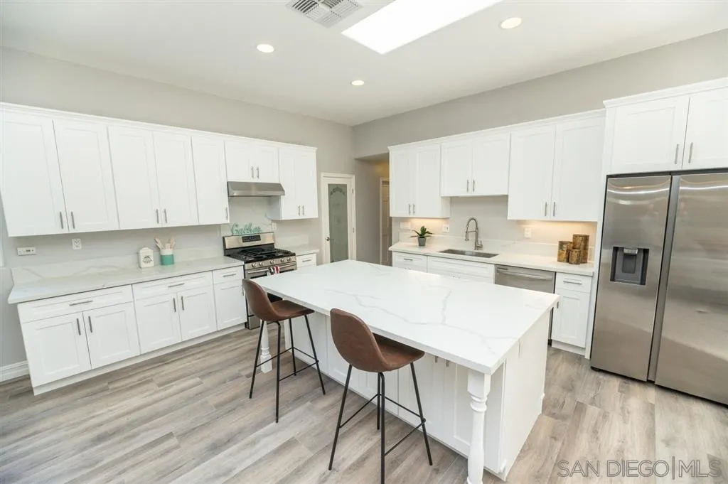 12841 Stone Canyon Road Poway, CA 92064 - Photo 7 of 25 a kitchen with a refrigerator a white stove top oven and white cabinets with wooden floor