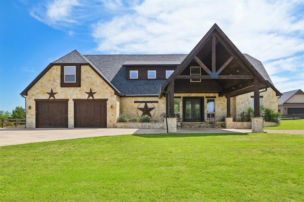 2085 Switzer Road Sanger, TX 76266 - Photo 2 of 39 Stone-clad exterior featuring a prominent covered entry with dark wood beams, a two-car garage with wood-finish doors, and multiple dormer windows