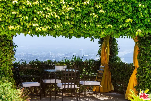 a view of a patio with couches table and chairs under an umbrella with potted plants