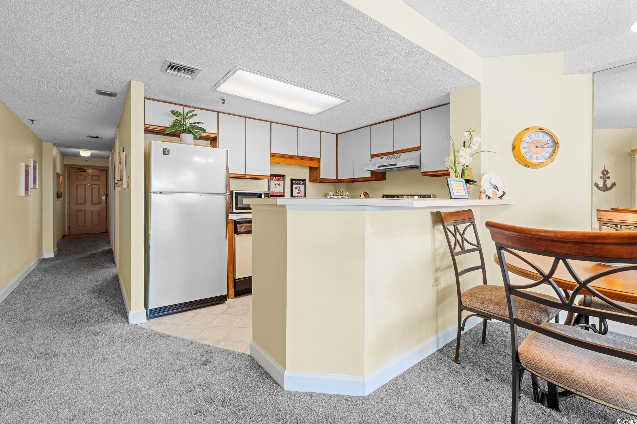 5511 North Ocean Boulevard, Unit 208 Myrtle Beach, SC 29577 - Photo 12 of 37 Kitchen with freestanding refrigerator, a textured ceiling, light countertops, light carpet, and a peninsula