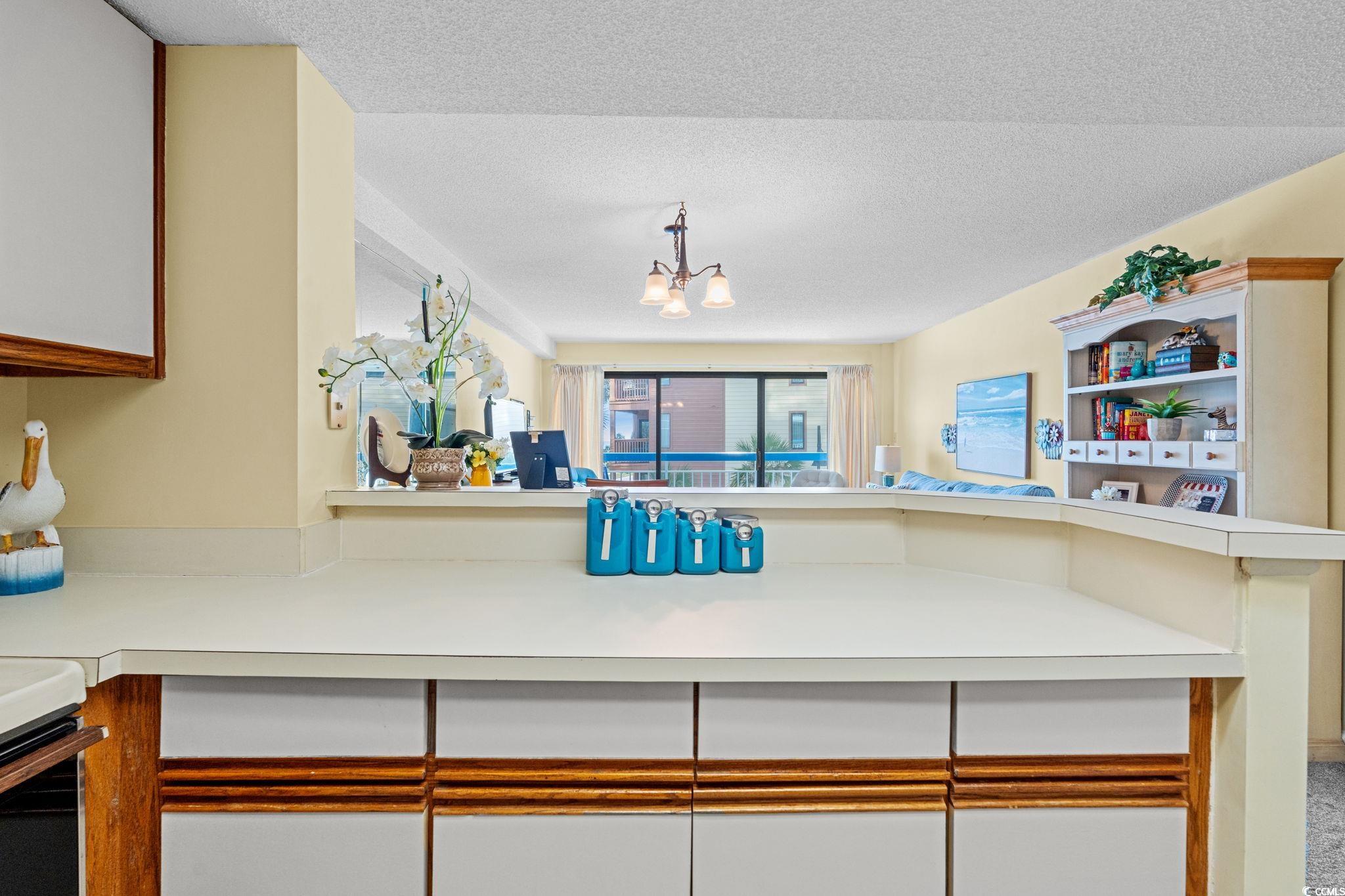 5511 North Ocean Boulevard, Unit 208 Myrtle Beach, SC 29577 - Photo 16 of 37 Kitchen featuring light countertops, a textured ceiling, a chandelier, a peninsula, and brown cabinetry