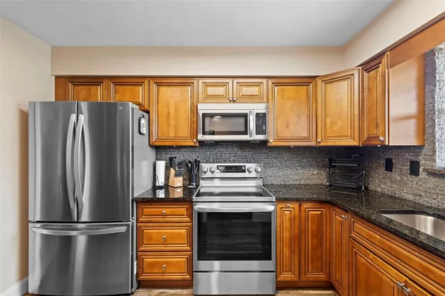 a kitchen with stainless steel appliances granite countertop a refrigerator a sink dishwasher a stove and white countertops with wooden floor