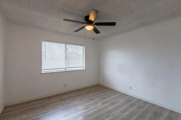 an empty room with wooden floor ceiling fan and windows