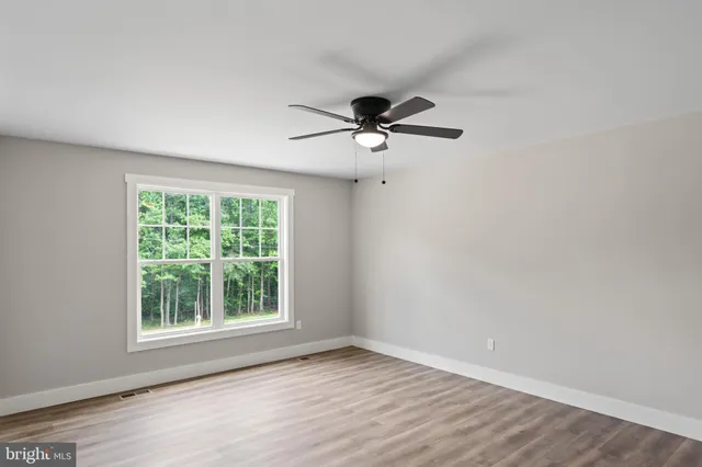 an empty room with wooden floor chandelier fan and windows