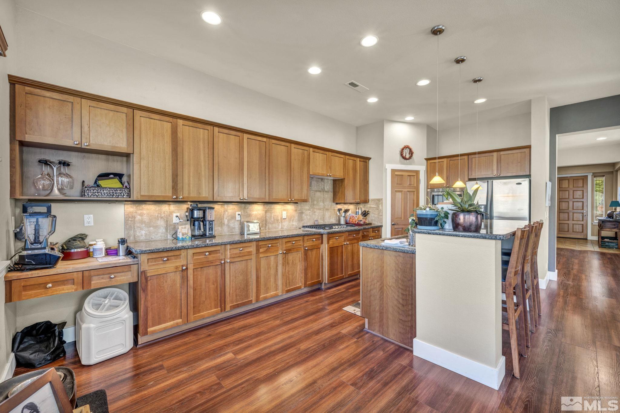 4975 Turning Leaf Way Reno, NV 89519 - Photo 8 of 40 a kitchen with kitchen island granite countertop wooden floors and white cabinets