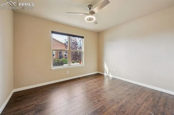 an empty room with wooden floor chandelier fan and windows