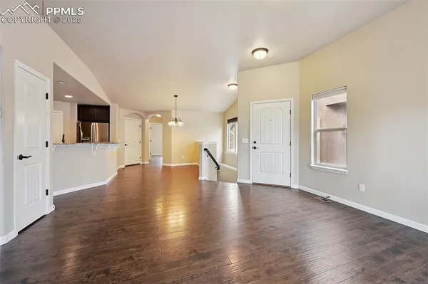 a view of an empty room with wooden floor and a kitchen