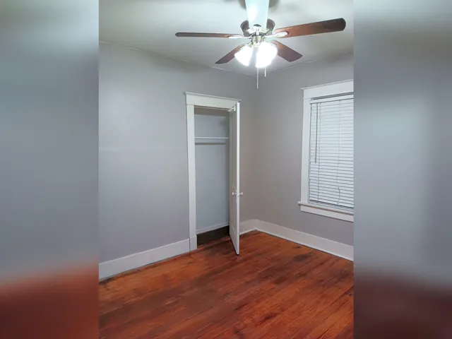 an empty room with wooden floor closet and fan