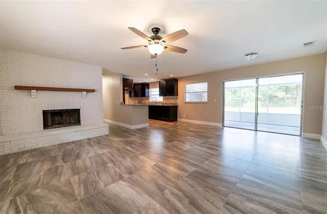 a view of a livingroom with a fireplace a ceiling fan and wooden floor