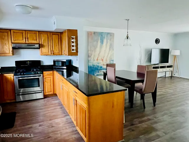 a kitchen with stainless steel appliances granite countertop a stove top oven a sink a dining table and chairs with wooden floor