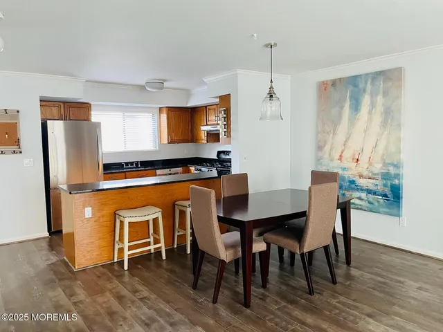 a kitchen with stainless steel appliances granite countertop a stove a refrigerator a sink a dining table and chairs with wooden floor