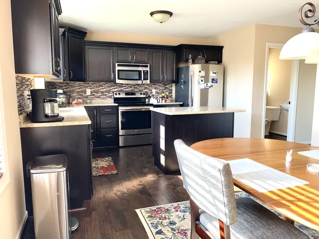 a kitchen with stainless steel appliances kitchen island granite countertop a sink dishwasher a stove and a refrigerator with wooden floor