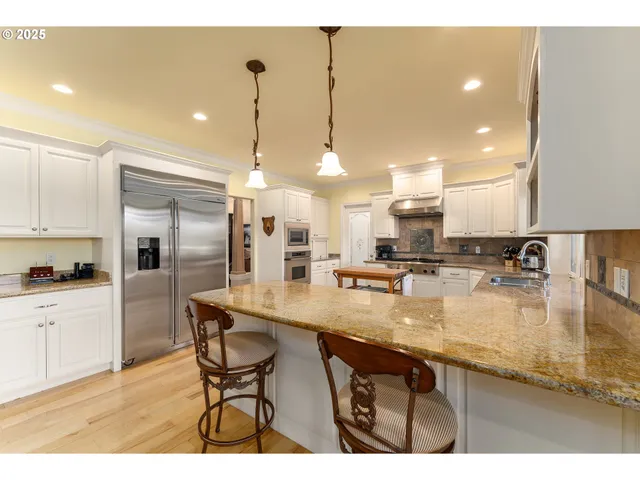 a kitchen with stainless steel appliances granite countertop a sink a stove a refrigerator and island with wooden floor