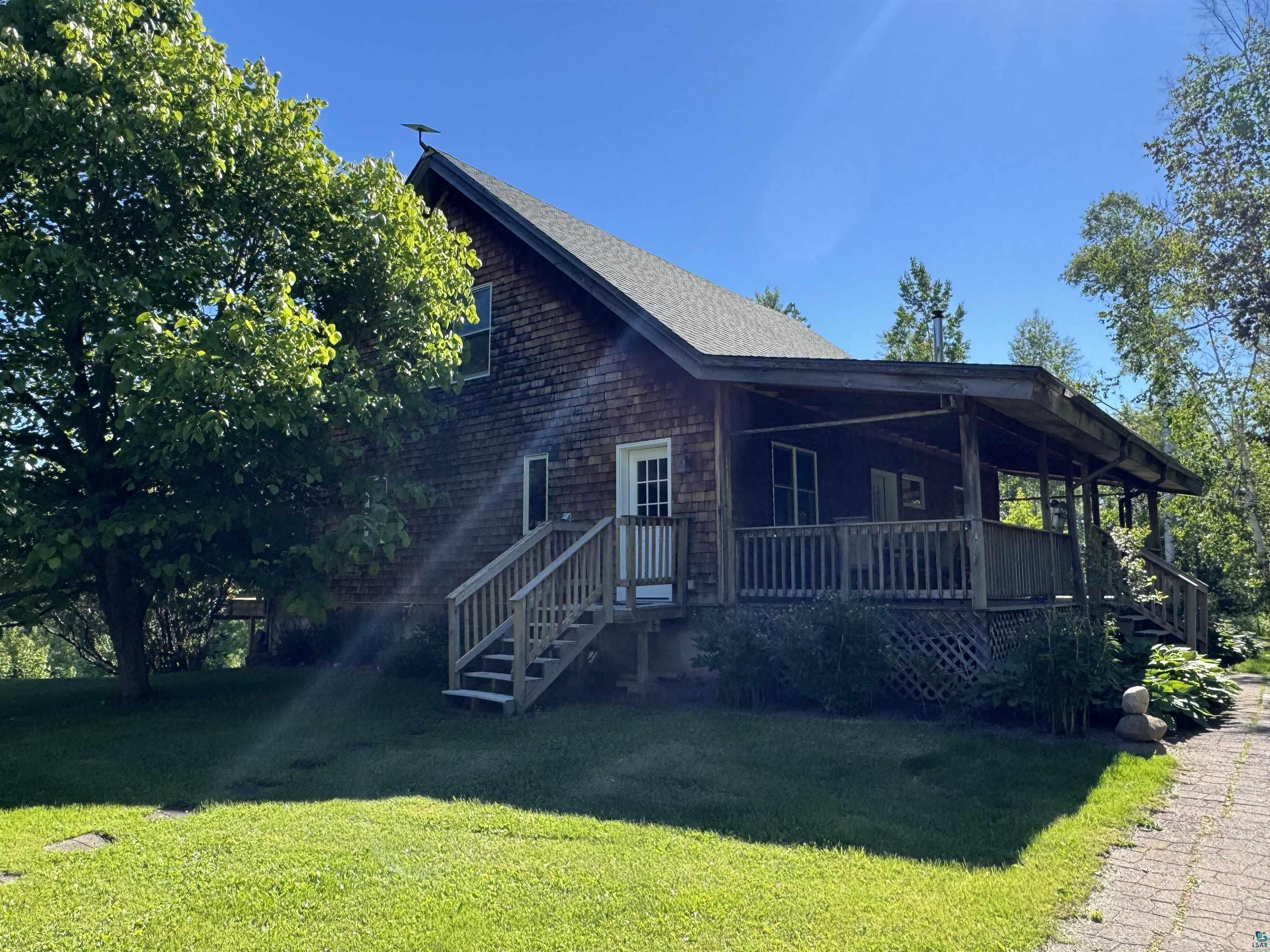 1745 Becks Road Maple, WI 54854 - Photo 3 of 50 Wood shake siding residence featuring an expansive covered porch, exterior wooden staircase, mature trees, and a paved walkway