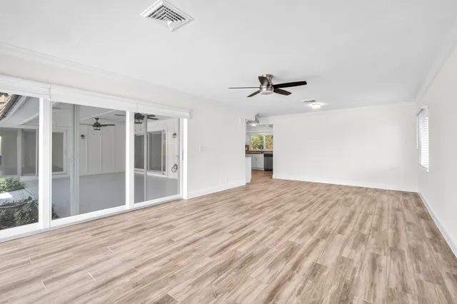a view of an empty room with wooden floor and a ceiling fan