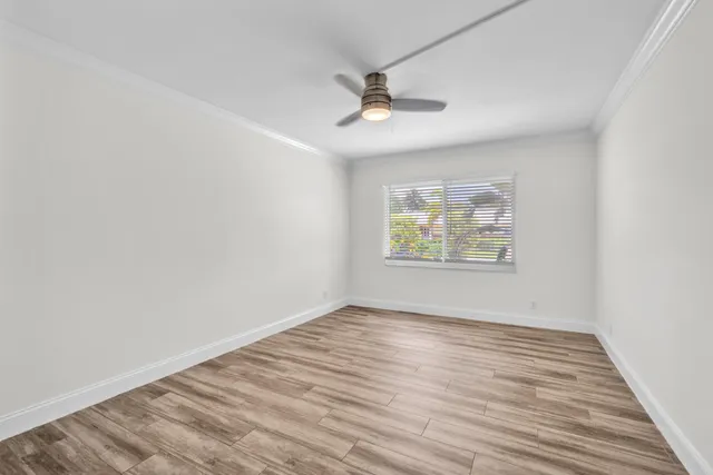 an empty room with wooden floor ceiling fan and windows