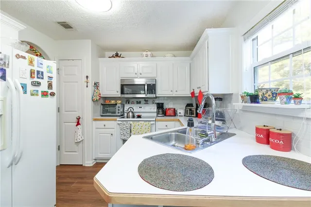 a kitchen with stainless steel appliances a stove a sink dishwasher a refrigerator and white cabinets with wooden floor