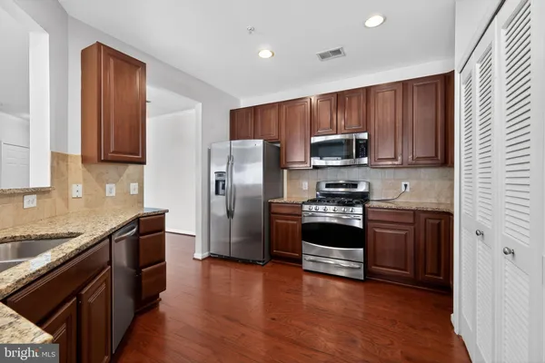 a kitchen with granite countertop wooden cabinets a stove a refrigerator and a sink with wooden floor