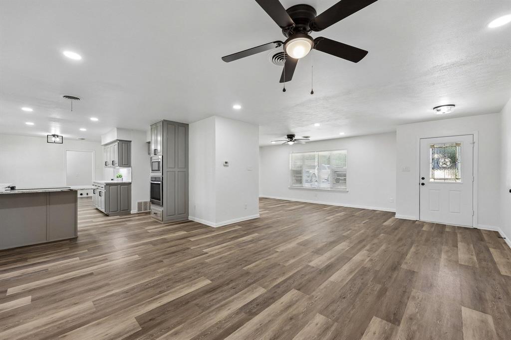 913 North Main Street Springtown, TX 76082 - Photo 7 of 25 an empty room with wooden floor a ceiling fan and kitchen view
