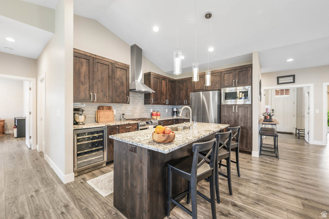 4527 North Seven Bridges Road Eden, UT 84310 - Photo 15 of 65 Kitchen featuring dark wood finish cabinets, light stone counters, beverage cooler, stainless steel appliances, and a kitchen bar