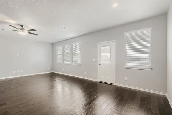 an empty room with wooden floor ceiling fan and windows