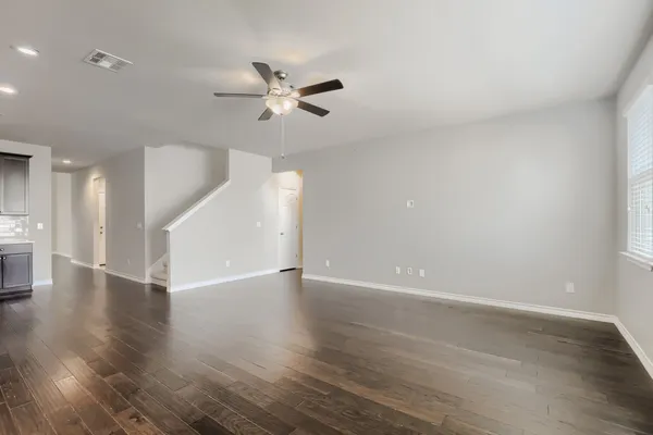 a view of an empty room with wooden floor and a ceiling fan