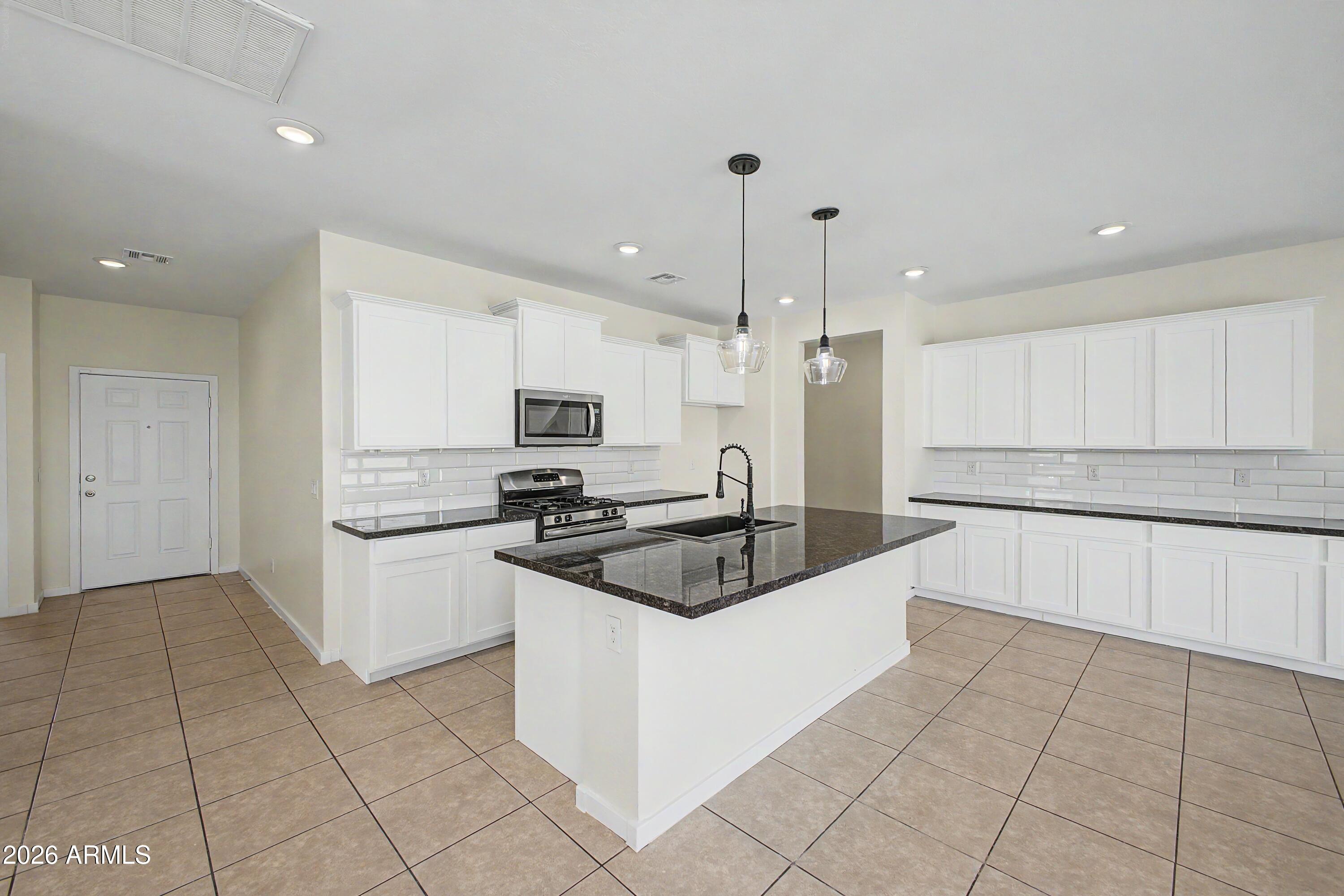 37154 North Navarra Road San Tan Valley, AZ 85140 - Photo 4 of 25 a kitchen with stainless steel appliances granite countertop a sink and a stove top oven with white cabinets