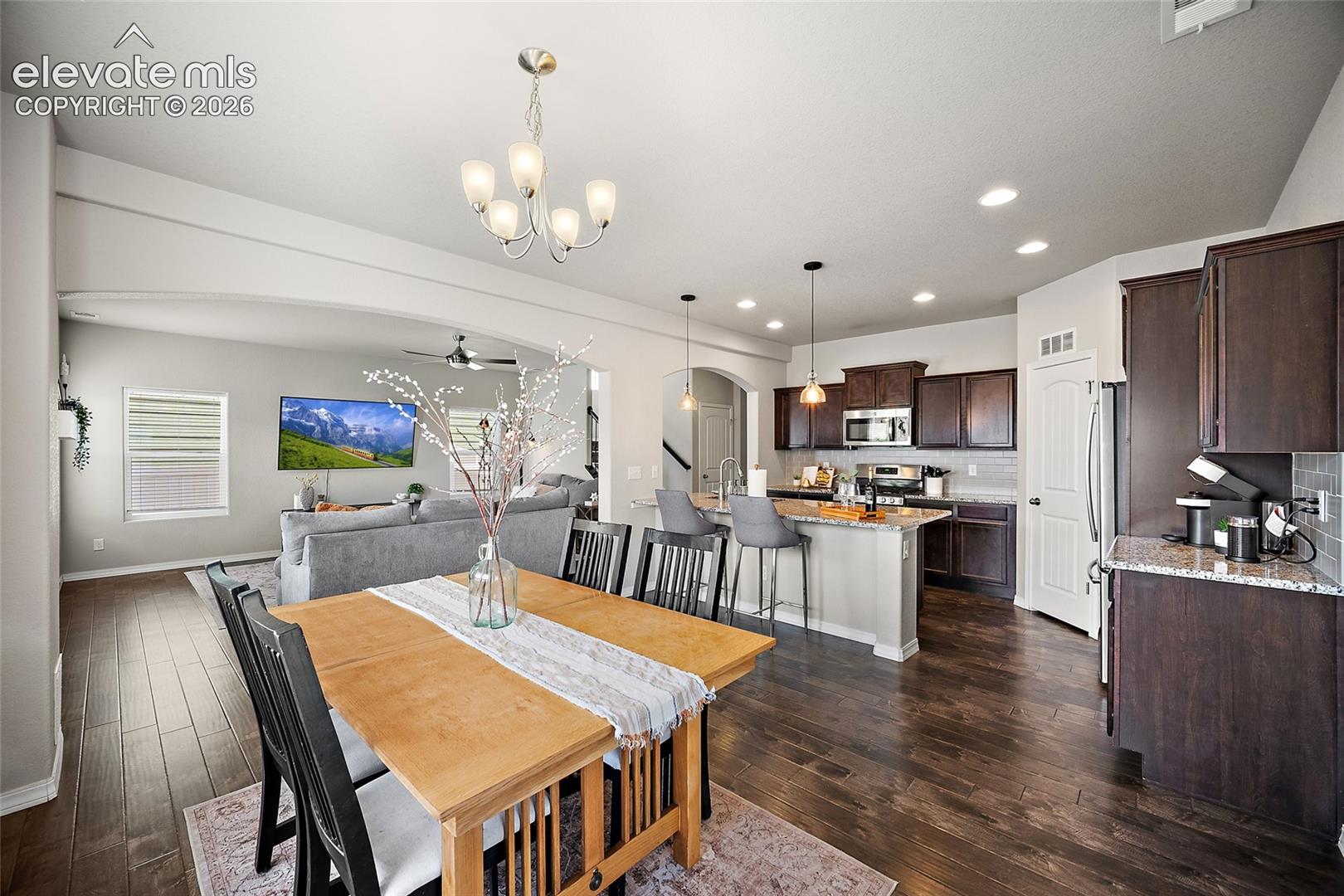 8675 Vanderwood Road Colorado Springs, CO 80908 - Photo 11 of 48 Open-concept layout featuring wood-finish flooring, a kitchen island with seating, dark wood cabinetry, and stainless steel appliances
