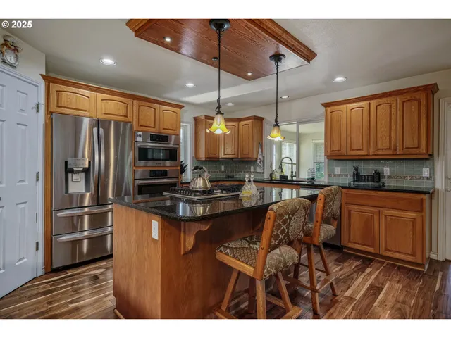 a kitchen with stainless steel appliances granite countertop a refrigerator a sink dishwasher a dining table and chairs with wooden floor